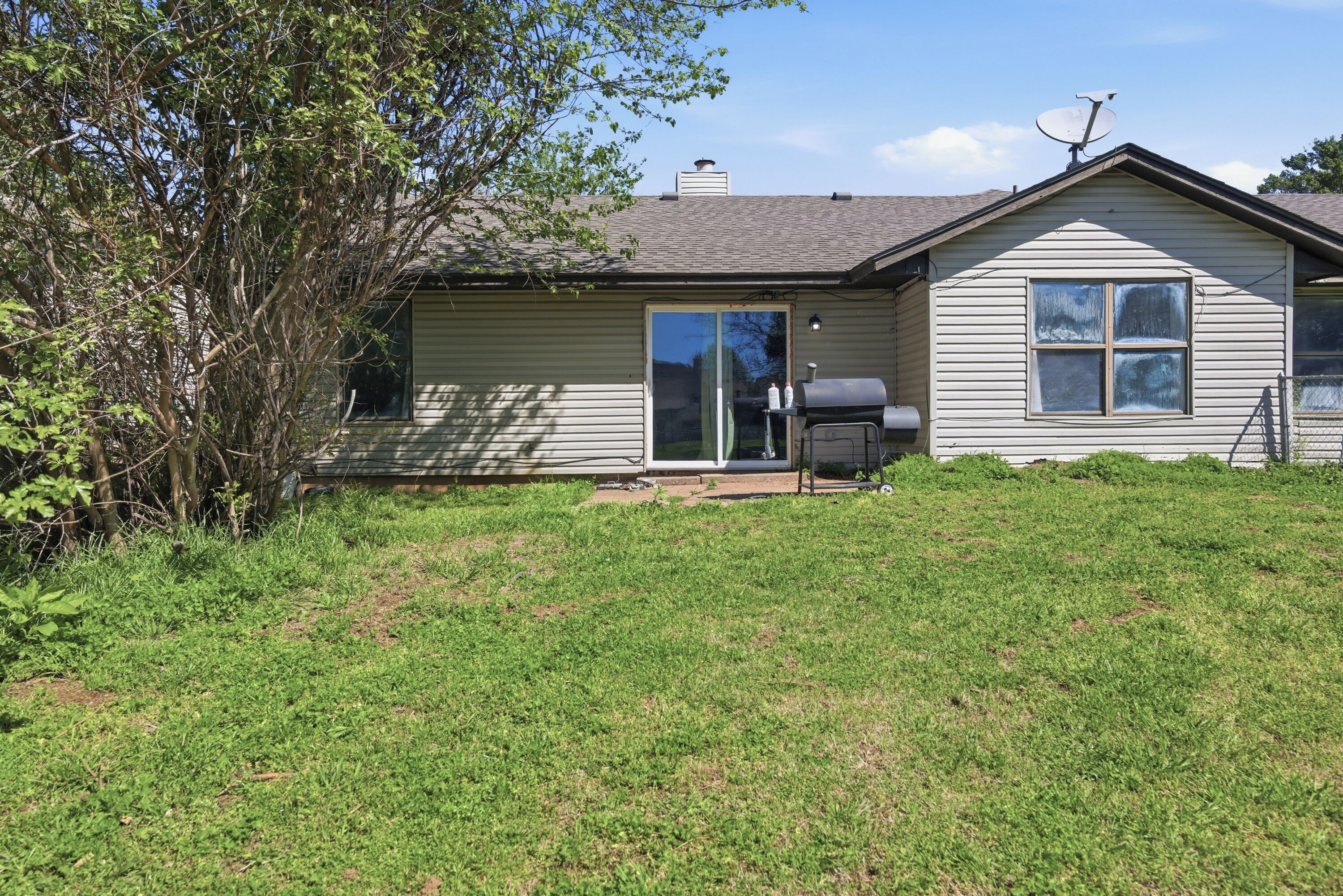 A single-story house with a sliding glass door, a patio with a grill, and a satellite dish.