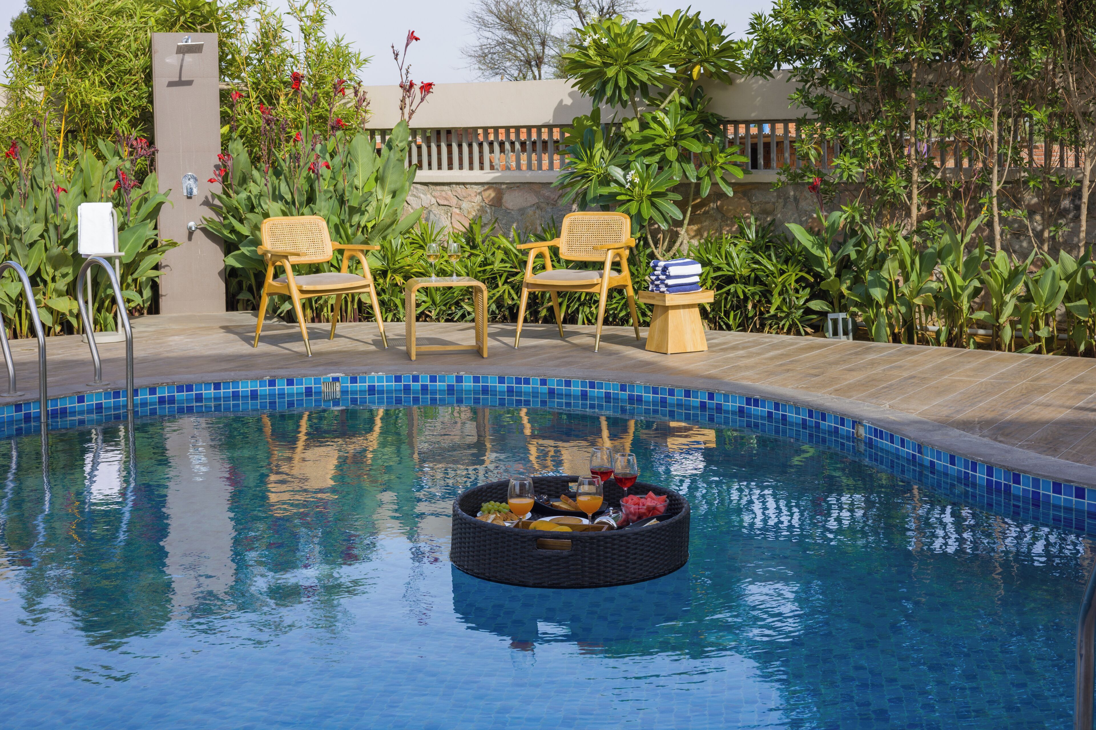 A pool with a floating tray of fruits and drinks, surrounded by chairs and a stone wall.