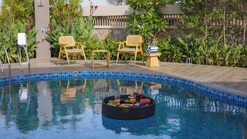 A pool with a floating tray of fruits and drinks, surrounded by chairs and a stone wall.