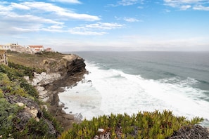 A coastal landscape with rocky cliffs, a beach, and a row of buildings.