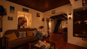 Una sala de estar acogedora con un sofá de madera, una mesa de centro con libros, una escalera y un estante en la pared con adornos.