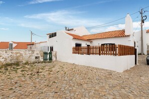 A white building with a tiled roof, a wooden fence, and a cobblestone courtyard.