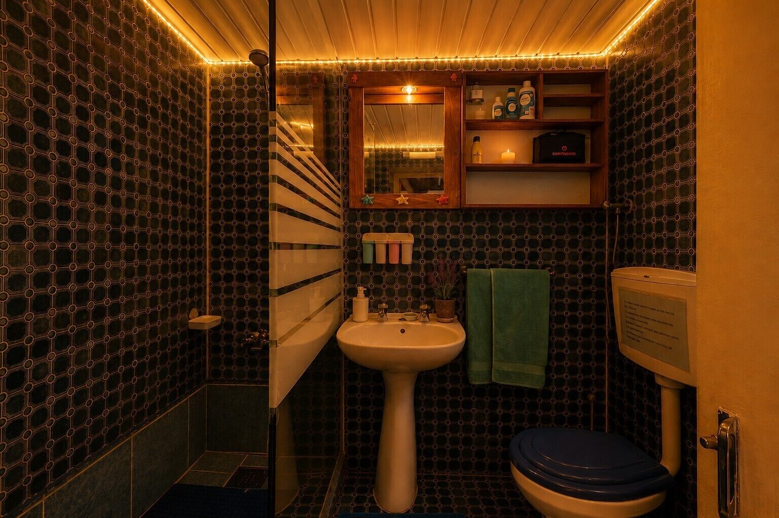 A compact bathroom with a sink, toilet, and shower area, featuring a patterned wall and warm lighting.