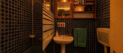 A compact bathroom with a sink, toilet, and shower area, featuring a patterned wall and warm lighting.
