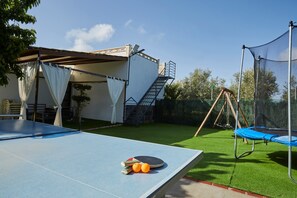Ein Pingpongtisch, ein Trampolin und eine Treppe, die zu einem überdachten Bereich führen.