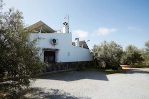 A building with a white exterior, a stone base, and a gravel driveway. - Villa 'Vega' with Mountain Views, Wi-Fi, and Air Conditioning (Pozo alcon jaen)