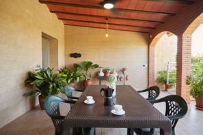 A covered patio area with a table set for two, surrounded by potted plants and a brick wall. - Villa 'Vega' with Mountain Views, Wi-Fi, and Air Conditioning (Pozo alcon jaen)