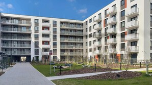 Un edificio residencial moderno de varios pisos con balcones, un patio central y un sendero para peatones.