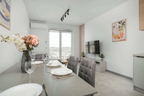 En spiseplads med et bord dækket til fire personer, en blomstervase og et moderne tv på væggen.