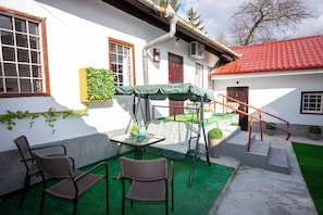 A patio area with a table and chairs, a swing set, and a staircase leading to a red-roofed building.