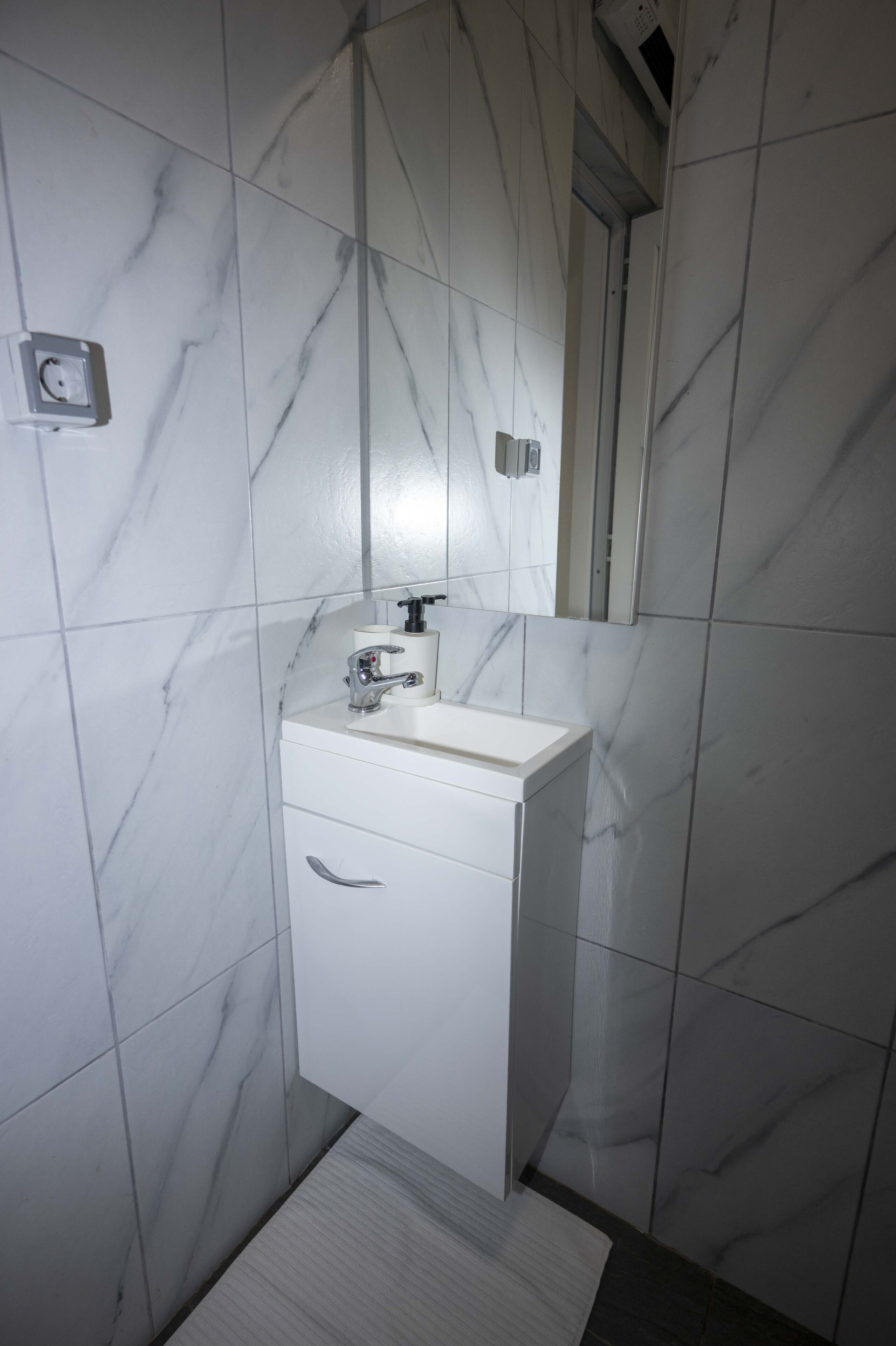 A bathroom with white marble tiles, a white sink, a mirror, and a towel rack.