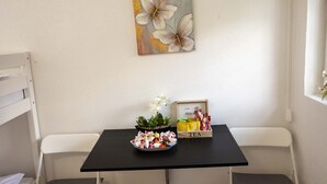 Une petite pièce avec un lit superposé, une table ornée d’un tableau représentant des fleurs, une boîte à thé et un climatiseur blanc.
