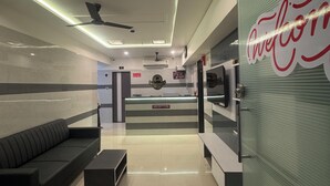 A reception area with a reception desk, a sofa, a ceiling fan, and a wall with a 'Welcome' sign. - Hotel Kalp Rooms (Vyara)