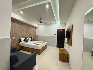 Une chambre d’hôtel moderne équipée d’un lit, d’un petit coin salon, d’une table d’appoint en bois, d’un ventilateur de plafond et d’un téléviseur fixé au mur.