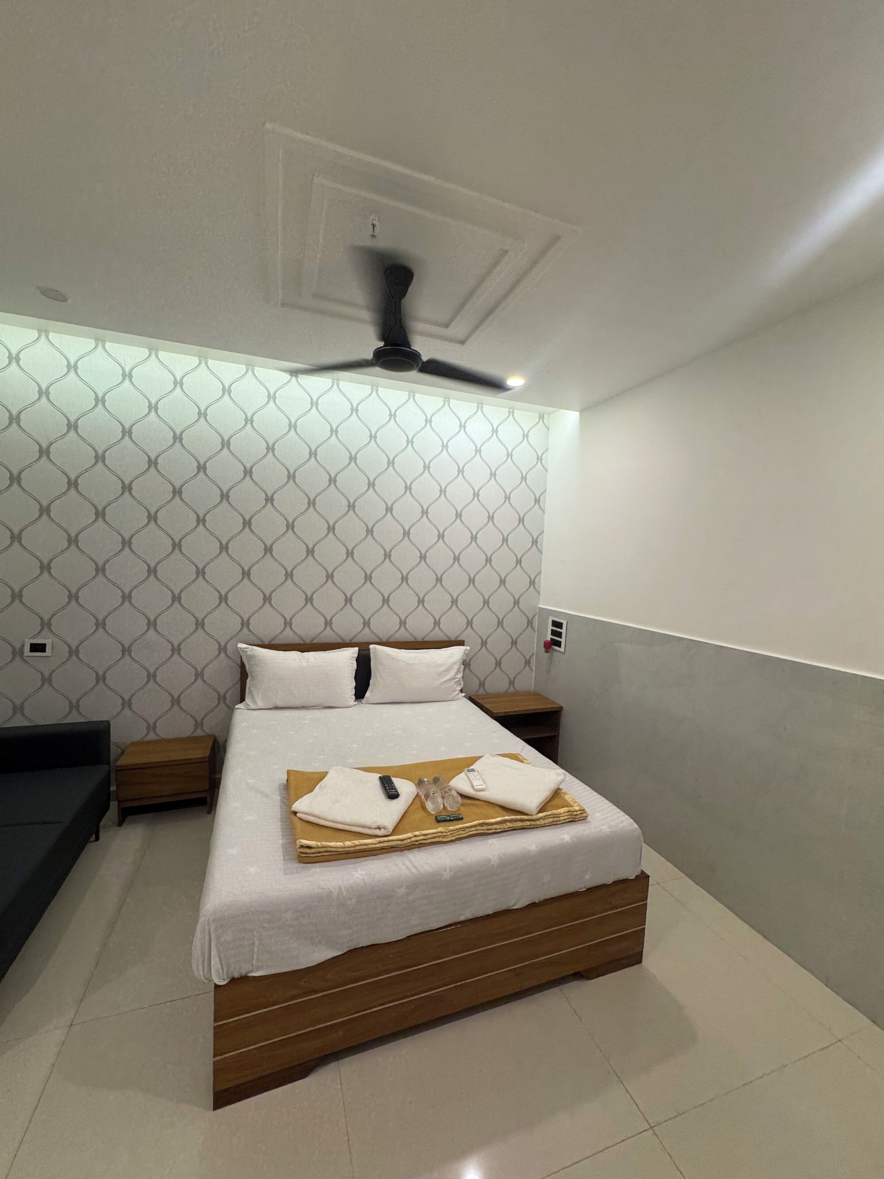 A neatly made bed with a wooden headboard, a bedside table, a small bedside table, and a ceiling fan.