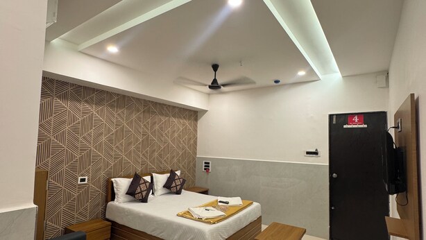 A modern hotel room with a bed, a seating area, a TV, and a door marked with the number 4. - Hotel Kalp Rooms (Vyara)
