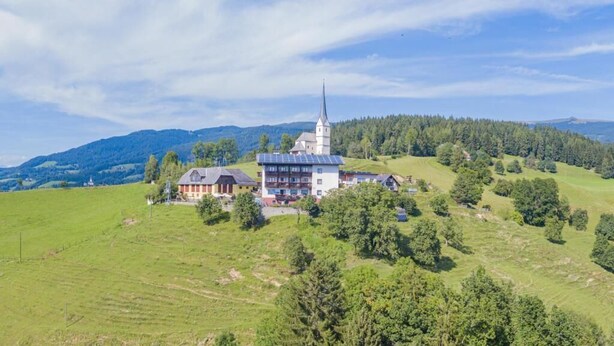A large building with a prominent tower, surrounded by green fields and trees. - Gasthof Gutmann (Eberstein)
