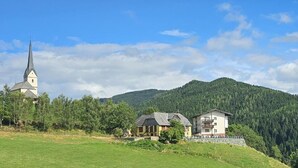 A church, a house, and a forested hill. - Gasthof Gutmann (Eberstein)