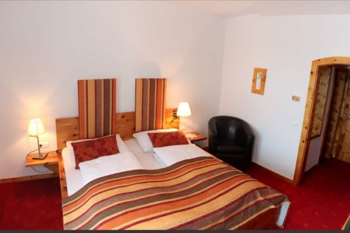 A hotel room with a bed, two bedside tables, a chair, a wooden headboard, and a door.