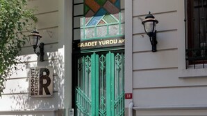En grön dörr med ett geometriskt mönster i ett färgat glasfönster, en skylt med texten ”SAADET YURDU AP” och en skylt med texten ”BOMONTI RESIDENCE”.