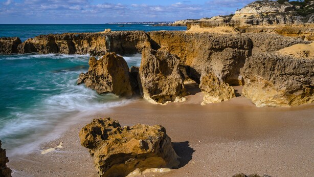 Eine felsige Küste mit klarem, blauem Meer und einem Sandstrand.