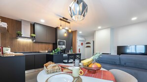 Eine moderne Küche mit Kochinsel, Essbereich mit rundem Tisch und ein Wohnzimmer mit Sofa und Fernseher.