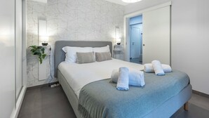 Ein modernes Schlafzimmer mit Bett, Nachttischlampen, einem Spiegel und einer Tür zu einem Badezimmer.