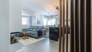 Ein modernes Wohnzimmer mit einem grauen Sofa, einem Esstisch und einer Küchenzeile im Hintergrund.