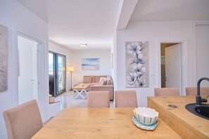 A modern living room with a sofa, a dining table, and a kitchen area with a sink. - Ray Holiday Apartment (Okrug Gornji)
