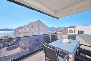 A balcony with a table and chairs, overlooking a cityscape and the sea. - Ray Holiday Apartment (Okrug Gornji)