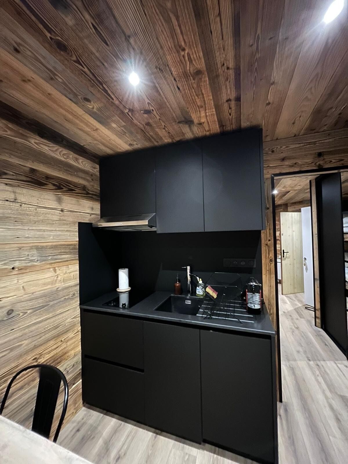 A modern kitchen with wooden ceiling beams, a black countertop, and a built-in stove.