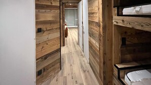Un interior de madera con una litera, un armario blanco y un pasillo que conduce a otra habitación.