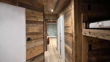 A wooden interior with a bunk bed, a white wardrobe, and a hallway leading to another room.