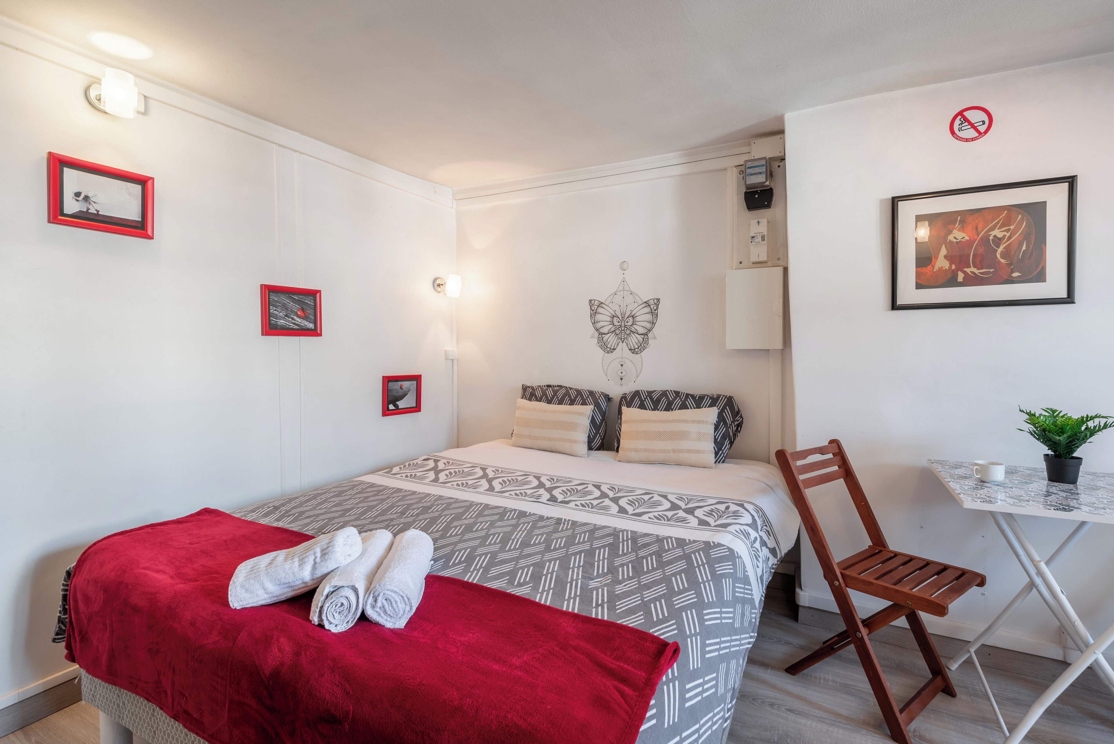 Une chambre bien rangée, avec un lit, une chaise, une petite table et des lampes fixées au mur.