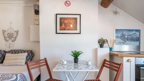 Une pièce confortable avec un lit, une table à manger entourée de chaises, un tableau encadré au mur et une petite plante posée sur la table.