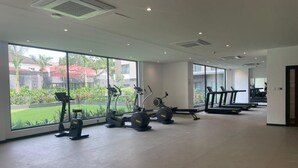 A gym with exercise equipment, large windows, and a view of greenery. - The Bantree by RoyalRest (Accra)