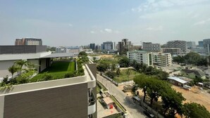 A high-rise building with a rooftop garden, a parking area, and a view of surrounding urban buildings. - The Bantree by RoyalRest (Accra)