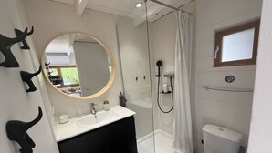 Un baño con ducha envuelta en vidrio, inodoro, lavabo con espejo y ganchos decorativos en la pared.