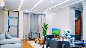 Ein modernes Wohnzimmer mit einer Couch, einem Esstisch, Stühlen, einem Fernseher und einer Pflanze.