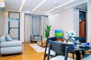 En moderne stue med sofa, spisebord, stole, fjernsyn og en plante.