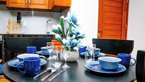 Ein runder Esstisch mit blauem Geschirr, eine Vase mit Blumen und eine Küche im Hintergrund.