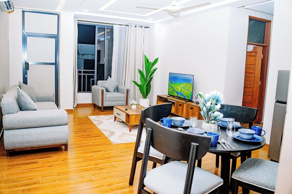 A modern living room with a sofa, dining table, chairs, and a television.