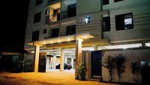 Ein mehrstöckiges Hotel mit überdachter Zufahrt, Parkplätzen im Freien und einem begrünten Außenbereich.