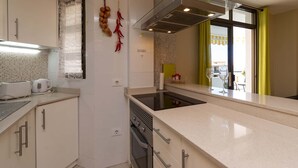 A modern kitchen with white cabinets, a built-in oven, a stainless steel range hood, and a window with yellow curtains. - Summerland 5 - 1 bedroom with terrace and pool view (Los Cristianos)