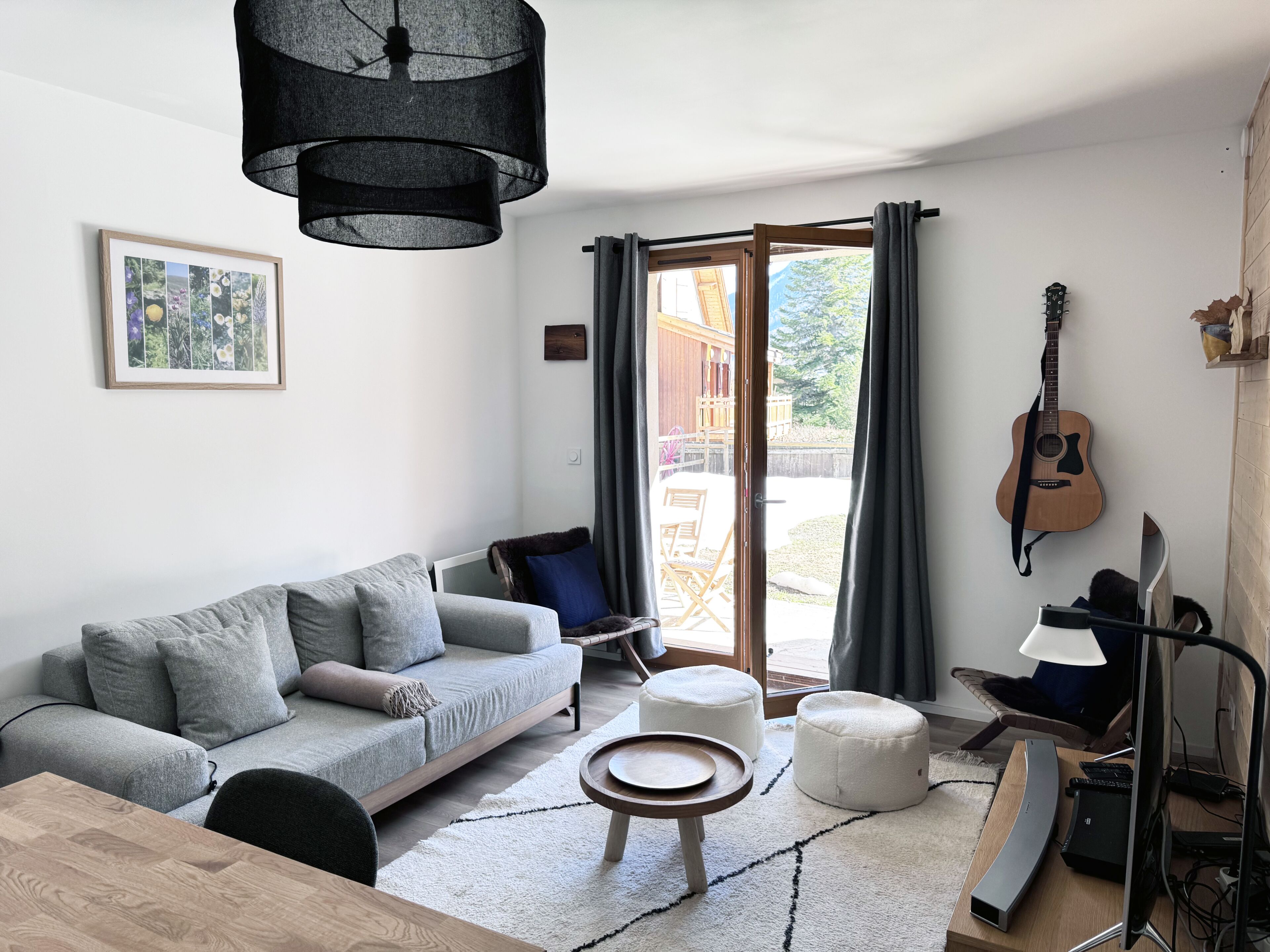 A modern living room with a grey sofa, a wooden coffee table, a white ottoman, a black lamp, a guitar, and a framed picture on the wall.