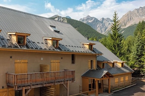 Un chalet doté d’un toit en pente, de balcons en bois et surplombant un paysage montagneux.