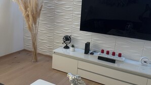 Ein modernes Wohnzimmer mit Flachbildfernseher, einem weißen Unterhaltungsschrank, einer dekorativen Pferdefigur und einem 'Welcome'-Schild.