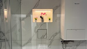 Ein Badezimmer mit Duschkabine aus Glas, Toilette, Waschbecken, Spiegel und Ablagefläche mit Topfpflanzen.