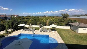 A swimming pool with lounge chairs and umbrellas, surrounded by greenery and a view of distant mountains.
