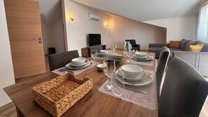 A dining area with a wooden table set for four, a woven basket, and a grey sofa in the background.
